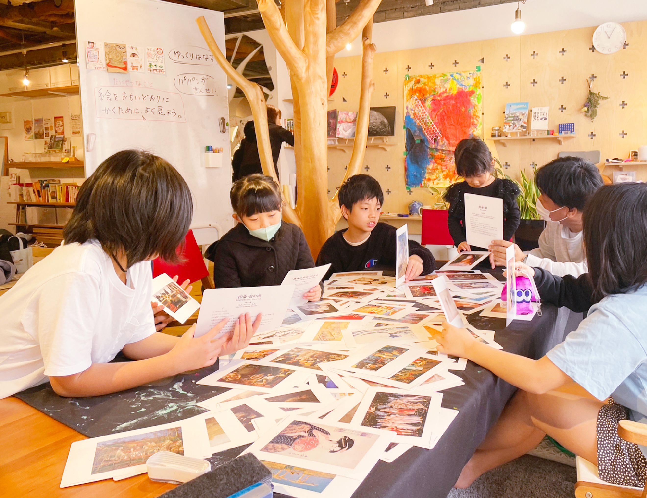 机にたくさん置いてある絵画のカードを子供たちが手に取って観察している。パパンダ先生はその様子を見ている